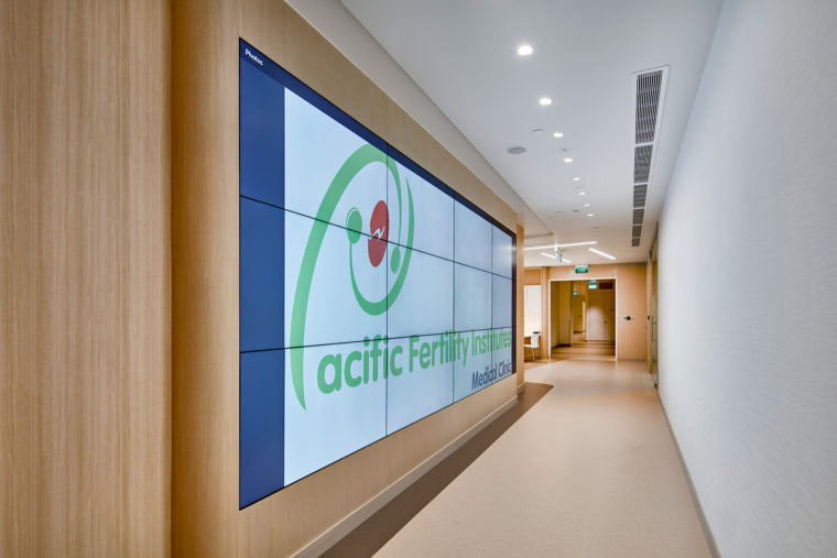 Pacific Fertility Institutes Clinic. A moving image gallery visually shortens the passage leading to the visitor area. In contrast to the noise of the moving image, the neutral colour palette of the reception provides an inviting and quiet mood, setting the patient at ease.