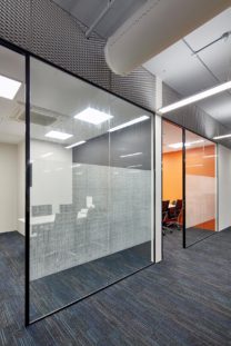 Acromec Ltd Offices. Director's offices align to the core wall. The overall aesthetic is industrial, with an exposed soffit, fabric ducts, cable trays and trunking. Expanded mesh panels above the rooms screen the acoustic baffles.