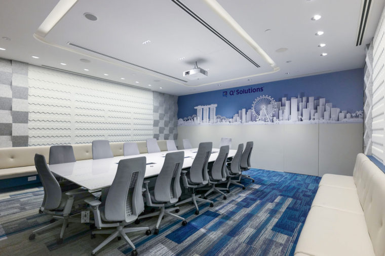 Q2 Solutions main conference room in Singapore. The high performance space dominated by a large white conference table delivers a shadowless meeting with low reverberation and high audibility. Bold blue colours and waterfall acoustic panel details provide visual interest.