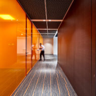 Acromec Ltd Offices. One of the key spaces of the facility is the corridor that connects the client interaction area to the main office. The walk is invigorating as the orange glass reflects off the laminate panelling.