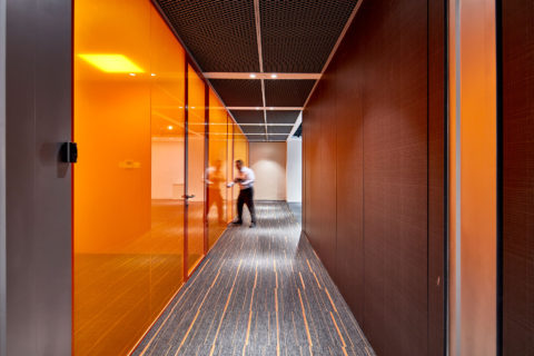 Acromec Ltd Offices. One of the key spaces of the facility is the corridor that connects the client interaction area to the main office. The walk is invigorating as the orange glass reflects off the laminate panelling.